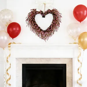 Heart-shaped twig wreath with pink accents hanging above a decorated white fireplace