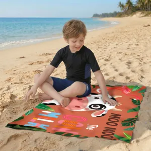 Detailansicht eines Mikrofaser-Strandtuchs mit Kuh-Motiv auf feinem Sandstrand.
