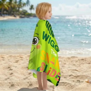 Kind am sonnigen Strand eingewickelt in ein grünes Cartoon-Mikrofaser-Strandtuch