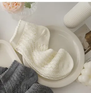 Detailed flat lay close-up of Japanese lace hollow mesh socks in ivory and grey tones.
