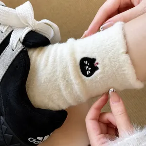 Close-up detail of white plush fuzzy warm mid-tube socks featuring cute cat embroidery design.