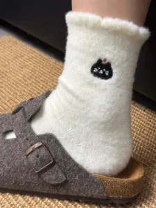 Close-up view of fluffy white mid-tube socks featuring cute embroidered black cat details.