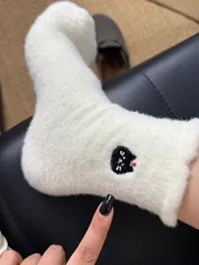 Fluffy winter socks detail, cozy white plush material with cute black cat embroidery design.