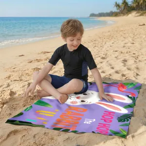Kind sitzt auf einem lila Mikrofaser-Strandtuch mit niedlichem Hasen- und Flamingo-Motiv