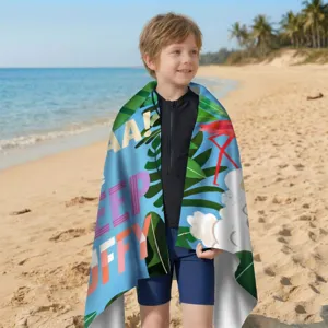 Ein kleiner Junge am sonnigen Strand, eingehüllt in ein buntes Tropen-Mikrofaserhandtuch