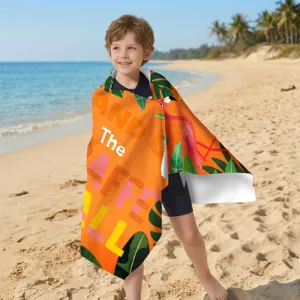 Kind am Strand in einem orangefarbenen Mikrofaser-Strandtuch mit Flamingomotiv eingewickelt