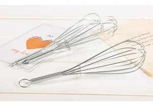 Close up of manual stainless steel wire egg whisk with spring handle for kitchen baking.