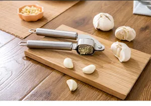 Nahaufnahme einer Edelstahl-Knoblauchpresse auf einem Holzschneidebrett mit Knoblauch.