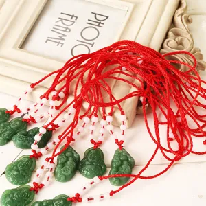 Pendentif Bouddha vert en imitation de jade avec un cordon rouge et des perles blanches.