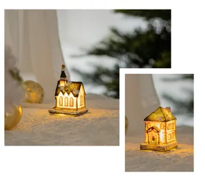 Close-up of cozy resin Christmas house with warm internal LED lighting on snow