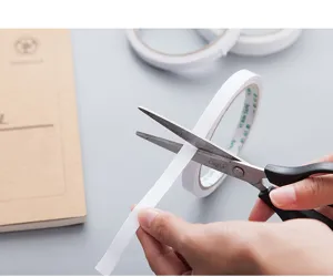 Detail shot of white double-sided adhesive tape being cut with scissors for office use.