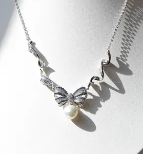 Elegante collar de lazo plateado con micro-piedras y colgante de perla blanca