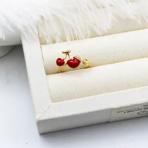 Detailed macro view of a 3D red enamel cherry ring displayed on a cream fabric tray
