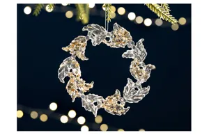 Close-up of transparent acrylic Christmas wreath ornament with gold sequins and bokeh lights