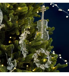 Close-up of transparent acrylic violin and angel ornaments hanging on a lit Christmas tree.