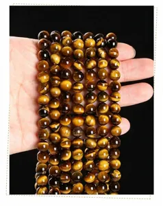 Détail macro de perles rondes en œil de tigre jaune naturel 7A sur main pour bijoux