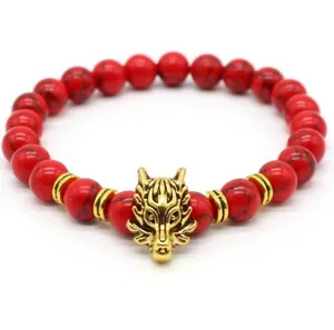 Dettaglio del bracciale di perle rosse con ciondolo a testa di lupo dorato e anelli distanziatori.