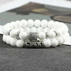 Detailopname van witte kralen dubbele armbandset met metalen Boeddha-hoofd en buisbedels.