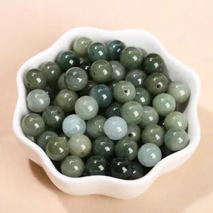 Perle rotonde in giadeite verde olio naturale in una ciotola bianca per gioielli fai da te