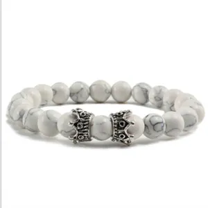 Vue détaillée du bracelet de perles en pierre blanche avec de charmants pendentifs couronne.