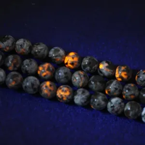 Macro shot of natural Yooperlite round beads with bright orange fluorescence under UV light