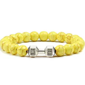 Gedetailleerde close-up van gele kraalsteenarmband met een zilveren fitness dumbbell bedeltje.