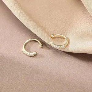 Nahaufnahme minimalistischer goldener Ohrklemmen mit funkelnden Kristallen auf Stoff.