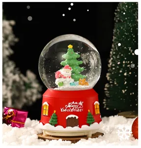 Weihnachtsschneekugel Detail mit Weihnachtsmann und beleuchtetem Baum auf rotem Sockel.