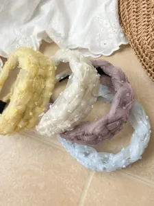 Primer plano de cuatro diademas trenzadas de malla en tonos pastel con una textura suave.