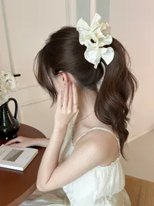 Detailed view of an elegant white ruffled satin hair clip with pearls on a ponytail.