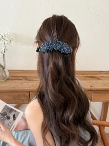 Détail d'une pince à cheveux banane élégante à pois bleus sur des cheveux bruns ondulés