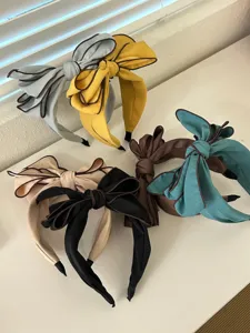 A detailed display of five elegant fabric bow headbands in various colors on a white shelf