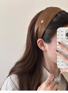 Close-up detail of a brown satin wide headband with elegant gold label on model.