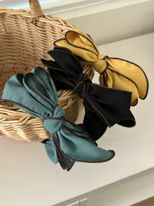 Close-up of three elegant fabric bow headbands in yellow, black, and teal colors