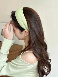 Close-up side view of a light green knitted wide headband on wavy brown hair