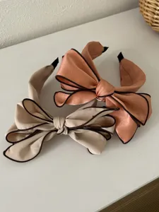 Detailed macro view of two stylish satin bow headbands in beige and peach coral