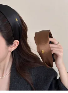 Close-up of elegant silk satin wide headbands in black and brown with gold metal tags.