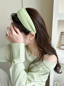 Close-up detail of a soft light green knitted wide headband worn by a model indoors.
