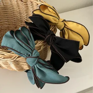 Three elegant wide bow headbands in teal, black, and mustard yellow with contrast piping.