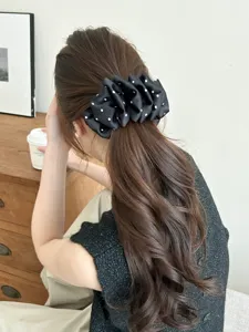 Close-up detail of a black polka dot bubble banana clip worn on wavy brown hair