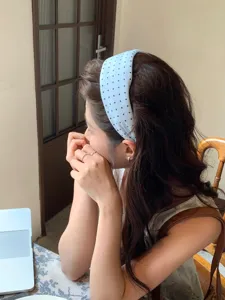 Close-up view of a model wearing a light blue polka dot wide headband in a lifestyle setting