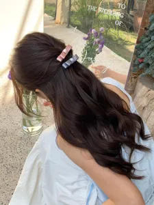 Detailed view of pink and blue satin bow hair clips styled on long wavy brown hair in garden.