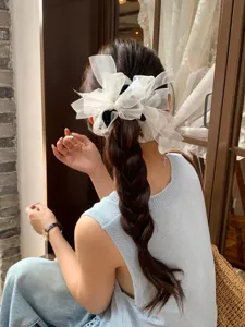 Vue arrière d'un modèle portant un grand chouchou nœud en organza blanc sur une tresse
