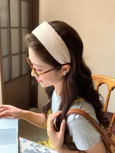 Side view of an elegant woman wearing a beige polka dot wide headband in a cafe