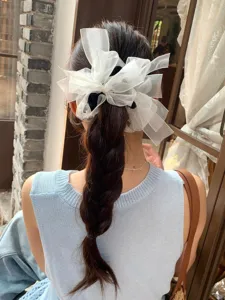 Gros plan d'un grand chouchou en organza blanc avec nœud et strass sur une tresse