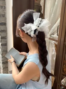 Gros plan d'un chouchou noeud en organza blanc avec strass sur une queue de cheval.