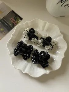Dettaglio di quattro mini mollette per capelli con fiocco a pois su un piatto bianco vintage