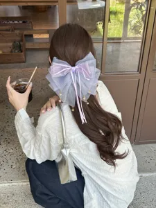 Vista detallada de una pinza para el pelo con lazo de malla morado sobre cabello ondulado.