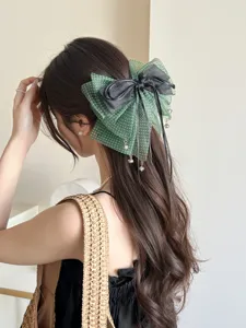 Detalle de una pinza para el pelo con lazo de lunares verdes y cintas negras colgantes.