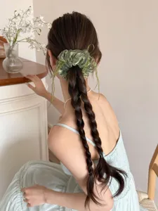 Detailopname van een groene organza scrunchie met lintstrik op een gevlochten kapsel
